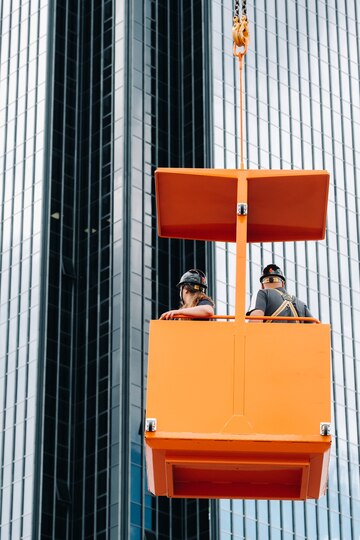 1 workers-construction-cradle-climb-crane-large-glass-building